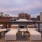 a deck with chairs and tables on it with buildings in the background